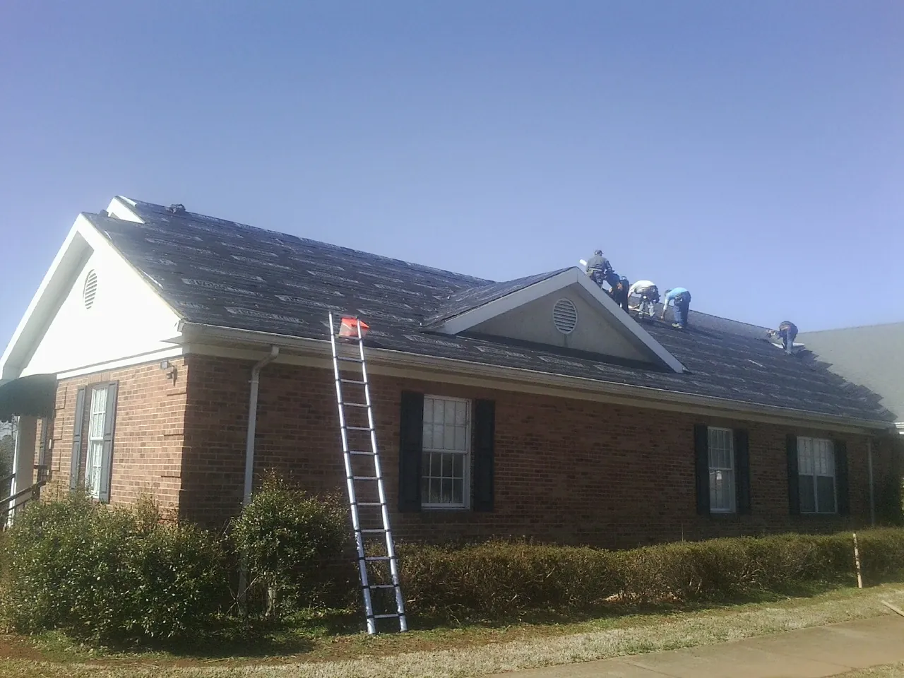 Crew tearing shingles off a brick ranch roof with a ladder set — Metal Roof Repair work by our crew in Pomeroy