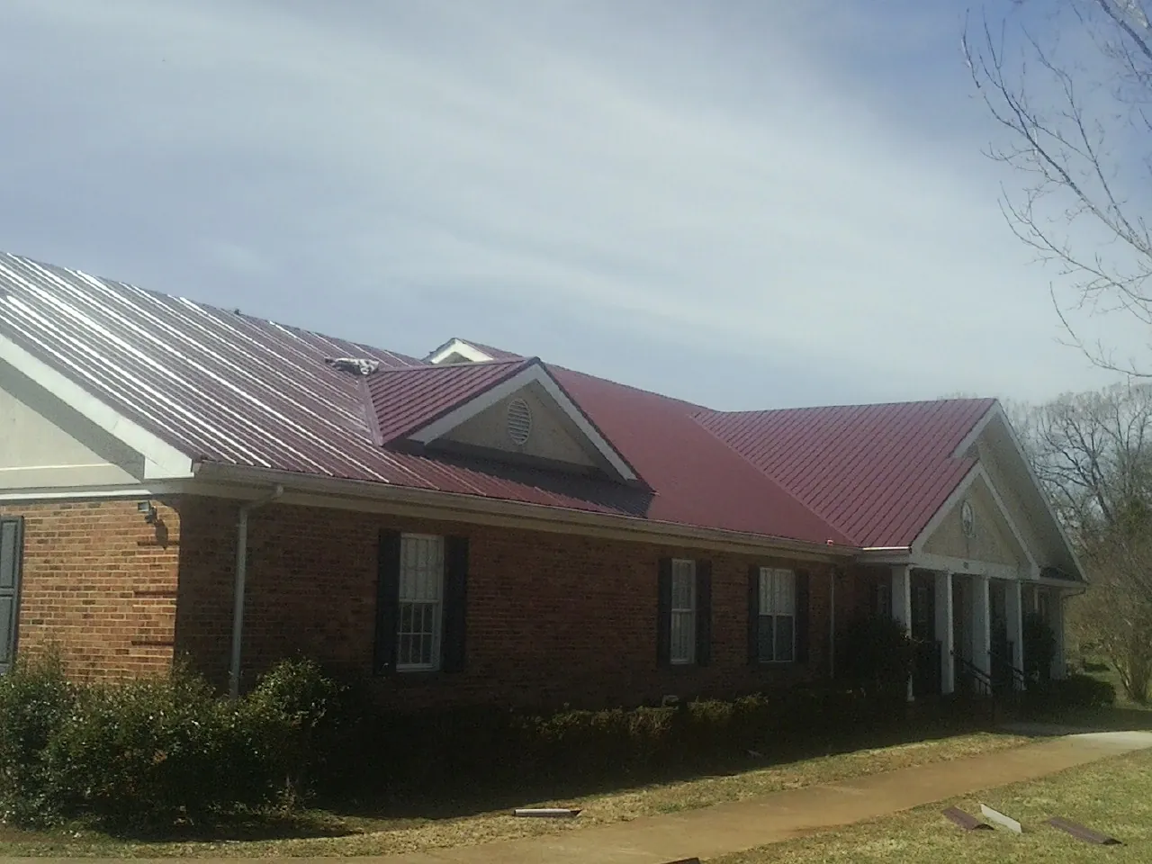Red metal roof with gabled entries on a long brick building, from a Hail Damage Roof Repair job in Pomeroy